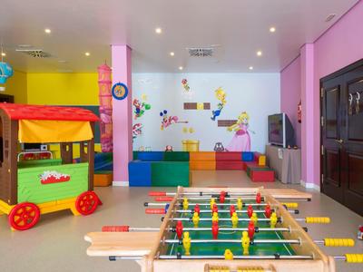 Espace de jeu intérieur coloré avec baby-foot, blocs mous et maisonnette dans une pièce lumineuse.