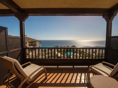Balcon avec des chaises donnant sur une plage ensoleillée et l'horizon de l'océan.