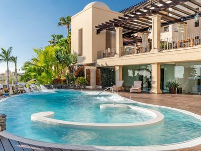 Piscine d'hôtel de luxe avec chaises longues, palmiers et ciel bleu clair.