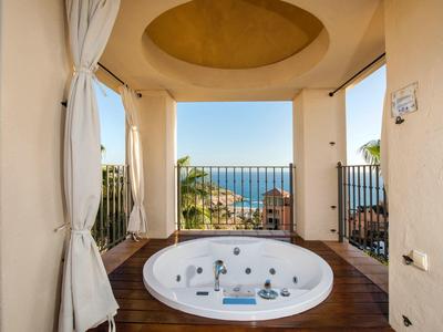 Jacuzzi extérieur avec vue sur l'océan, palmiers et plage, sous un plafond jaune incurvé.