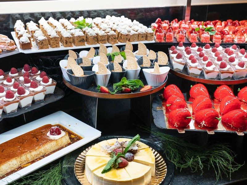 Assortiment de desserts élégants disposés sur des plateaux, comprenant des pâtisseries, gâteaux et fruits.