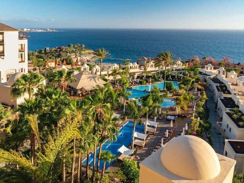 Complex avec piscines, palmiers, transats et vue sur l'océan au coucher du soleil.