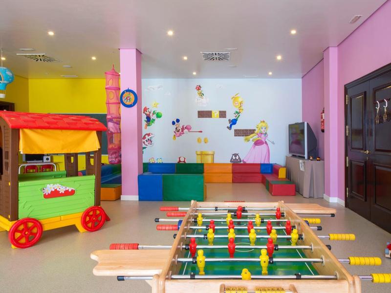 Espace de jeu intérieur coloré avec baby-foot, blocs mous et maisonnette dans une pièce lumineuse.