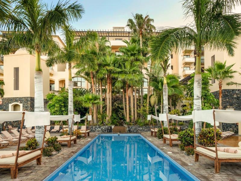 Piscine de resort entourée de palmiers, transats et végétation luxuriante dans un hôtel.