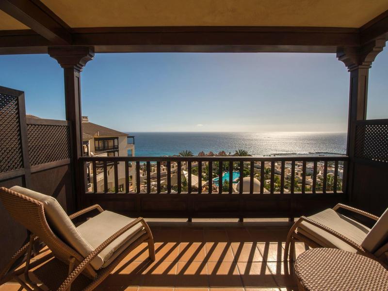 Balcon avec des chaises donnant sur une plage ensoleillée et l'horizon de l'océan.