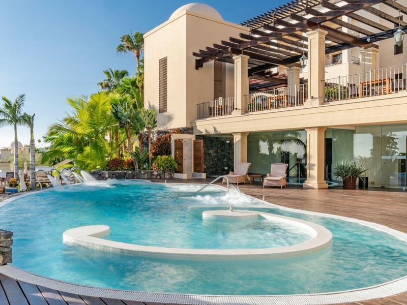 Piscine d'hôtel de luxe avec chaises longues, palmiers et ciel bleu clair.