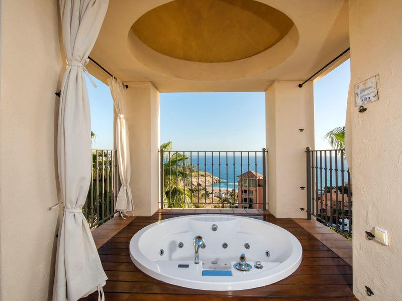 Jacuzzi extérieur avec vue sur l'océan, palmiers et plage, sous un plafond jaune incurvé.