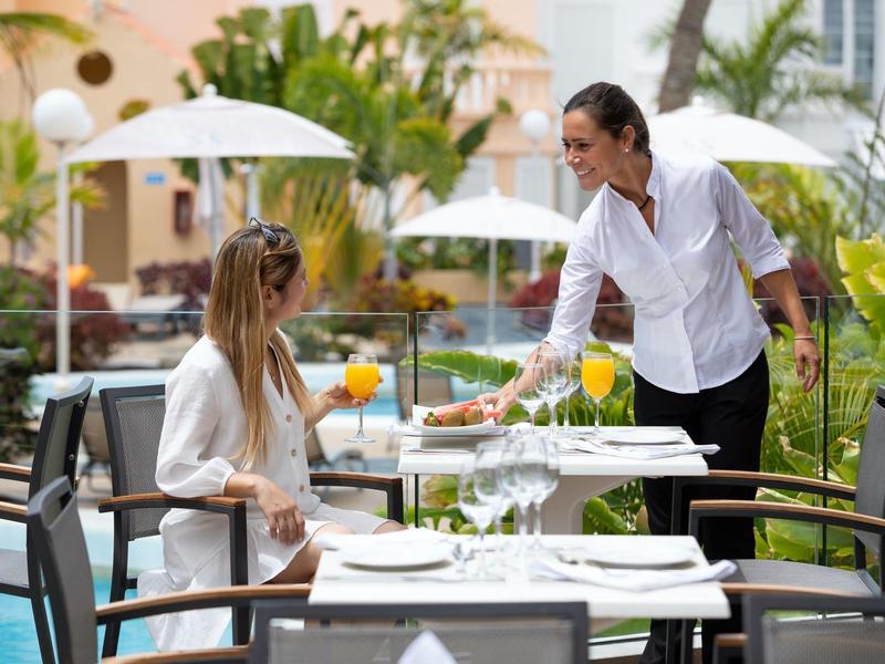 Un cameriere serve una bevanda a una donna a un tavolo apparecchiato nell'area esterna di un hotel.