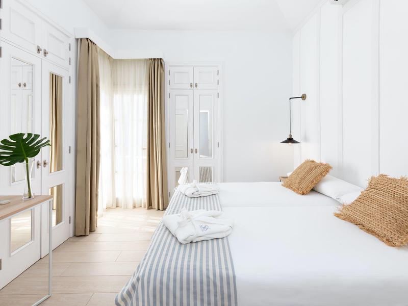 Camera d'hotel luminosa e moderna con letto matrimoniale, tende beige e arredamento minimalista.