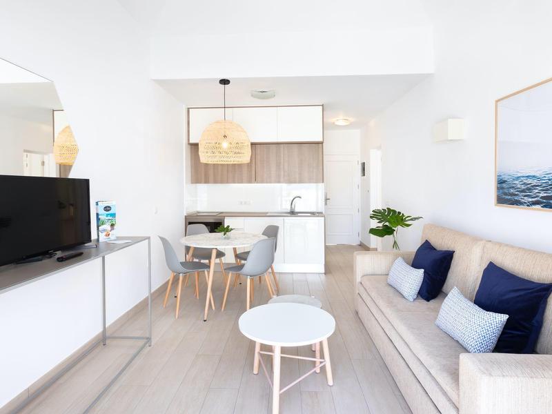 Luminoso soggiorno con divano, TV, zona pranzo e cucina moderna in un ambiente aperto.