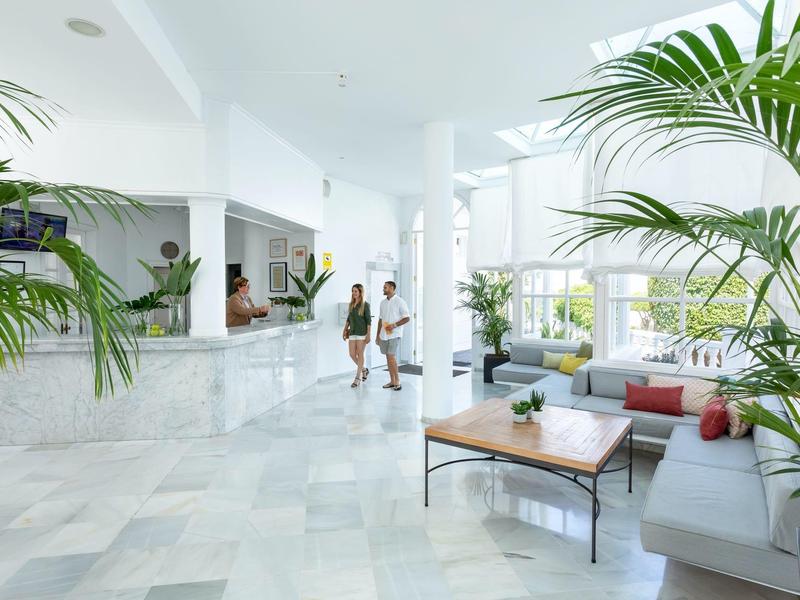 Luminoso e moderno ingresso dell'hotel con marmo bianco, piante e aree salotto accoglienti.