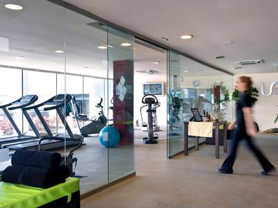 Nowoczesna siłownia hotelowa z bieżniami i sprzętem za szklaną ścianą.
