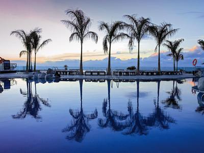 Spokojny basen odbijający palmy o zachodzie słońca przy plaży hotelowej