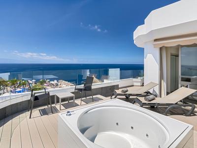 Balkon z jacuzzi, miejscami do siedzenia i widokiem na morze w słoneczny dzień.