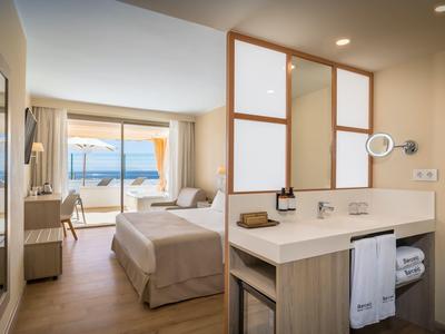 Moderní hotelový pokoj s výhledem na moře, pohodlnou postelí a umyvadlovou částí.