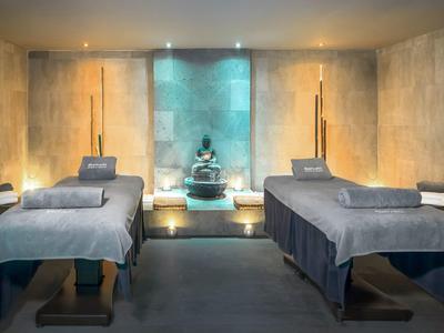 Dva masážní stoly v tlumeně osvětlené spa místnosti s sochou Buddhy.