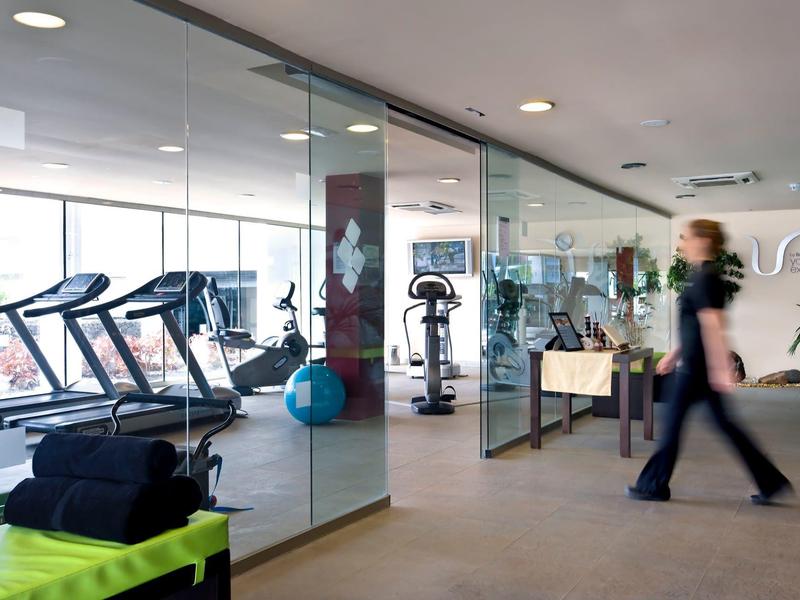 Moderní fitness místnost s běžeckými pásy, cvičebními stroji a skleněnými stěnami v hotelu.