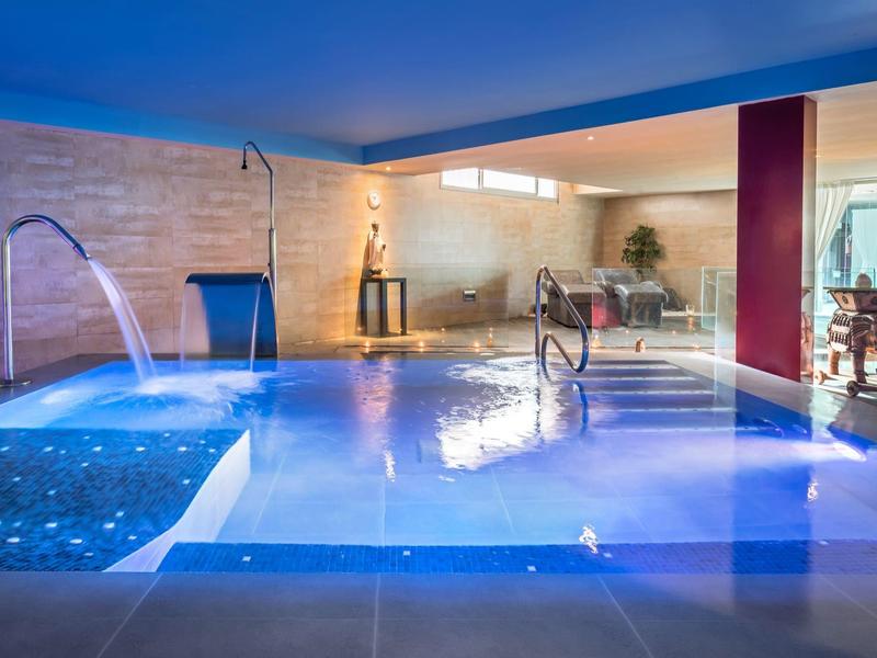 Moderní krytý bazén s vodními prvky a relaxačními posezeními v elegantním prostředí.