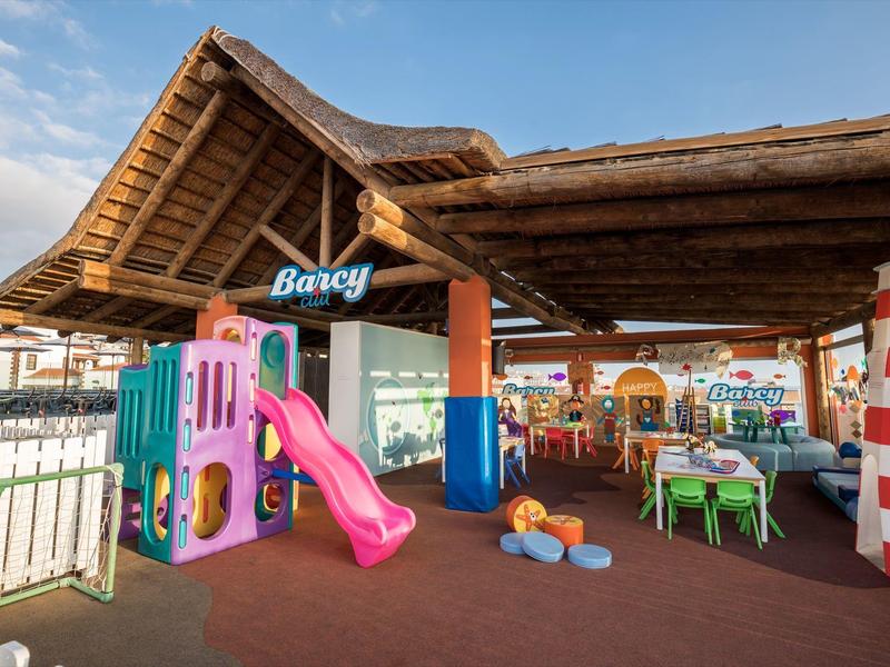 Barevná dětská zóna s klouzačkou a hračkami pod dřevěným pavilonem venku.