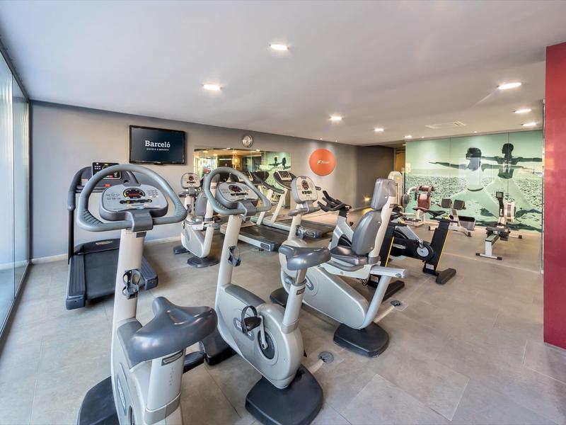 Moderní hotelové fitness s různými kardio stroji a velkými okny.