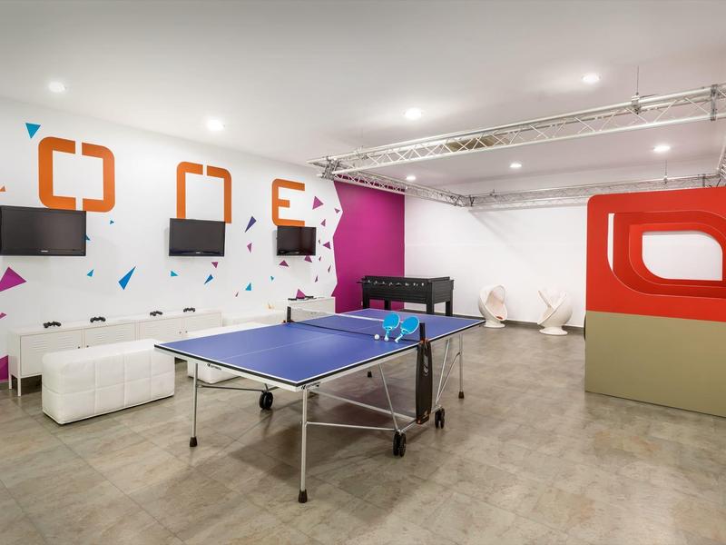 Moderní herna s pingpongovým stolem, pohovkami a barevným designem stěn.