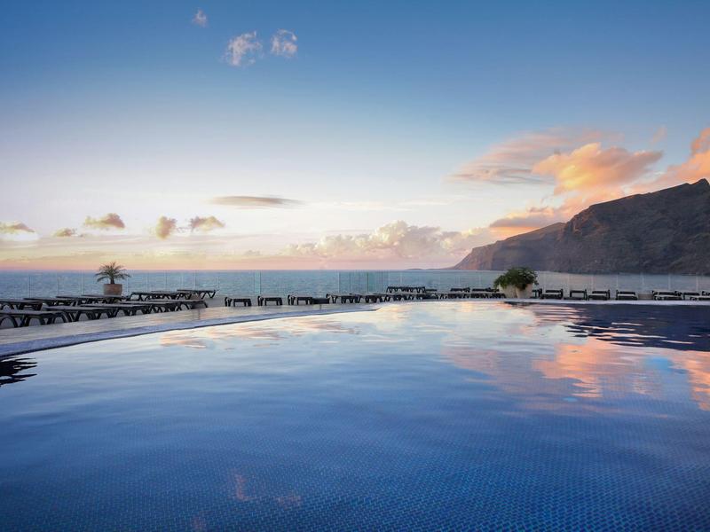 Infinity bazén s výhledem na moře a hory při západu slunce.