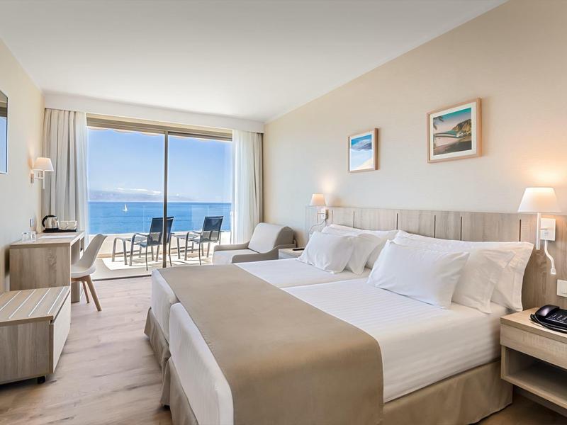 Moderní hotelový pokoj s manželskou postelí a balkonem s výhledem na moře
