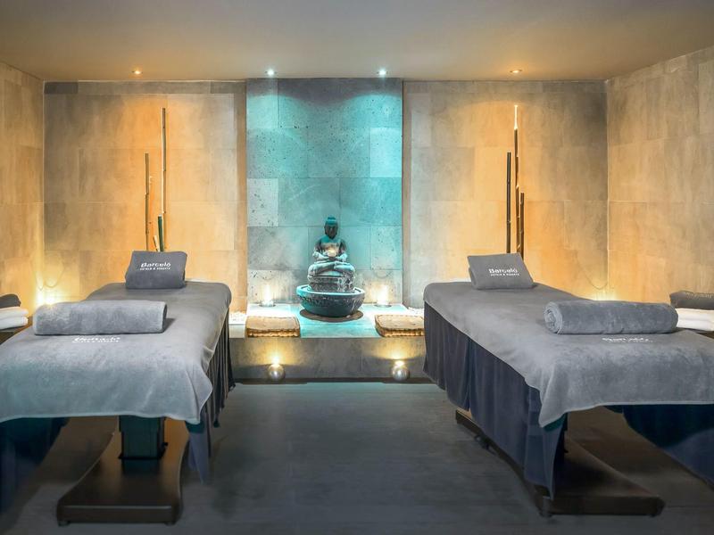 Dva masážní stoly v tlumeně osvětlené spa místnosti s sochou Buddhy.