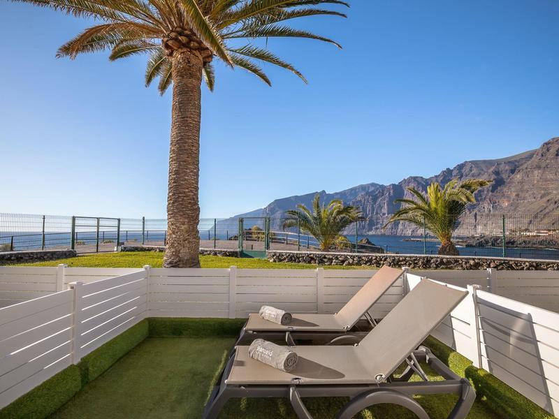 Dvě lehátka na terase s palmami a výhledem na moře a hory.