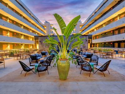 Cour intérieure d'hôtel avec coins salon et grande plante en pot au centre au crépuscule.