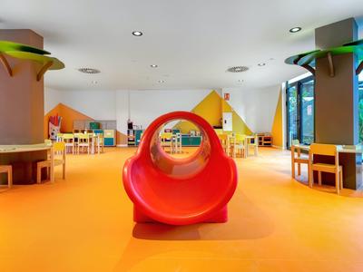 Heldere, kleurrijke speelruimte voor kinderen met glijbaan en meerdere tafels en stoelen.