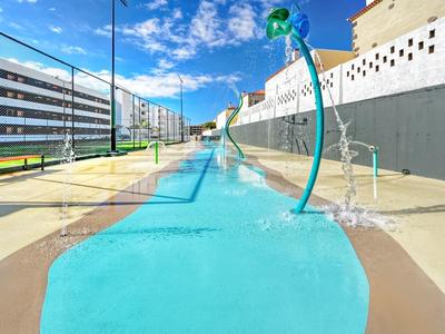 Modern waterspeelplaats met blauwe wateroppervlakken en groene waterdispensers op een zonnige dag.