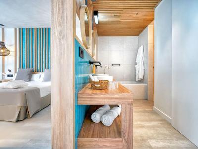 Licht hotelkamer met modern houten wastafelmeubel en uitzicht op de slaapkamer.