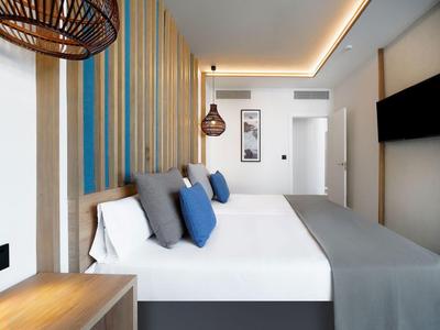 Moderne hotelkamer met een groot bed, blauwe kussens en een tv aan de muur.