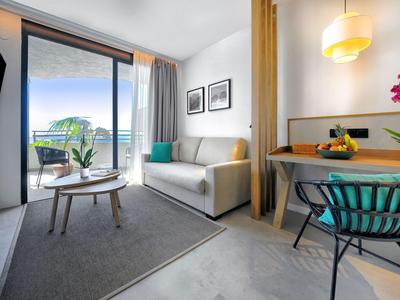 Chambre d'hôtel moderne avec balcon, canapé, table et chaises aux tons neutres.