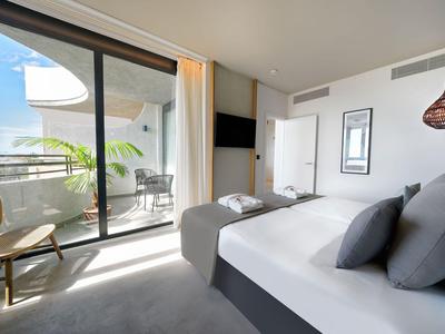 Chambre d'hôtel moderne avec grand lit, coin salon et balcon avec vue sur la mer.