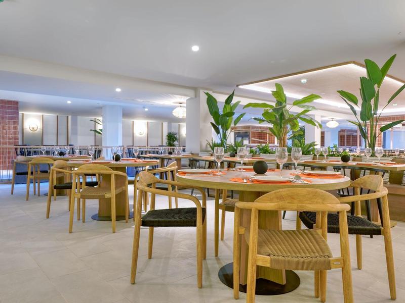 Moderne hotelrestaurant met houten tafels, stoelen en grote potplanten.