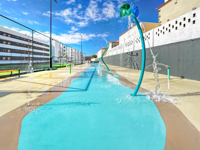 Modern waterspeelplaats met blauwe wateroppervlakken en groene waterdispensers op een zonnige dag.