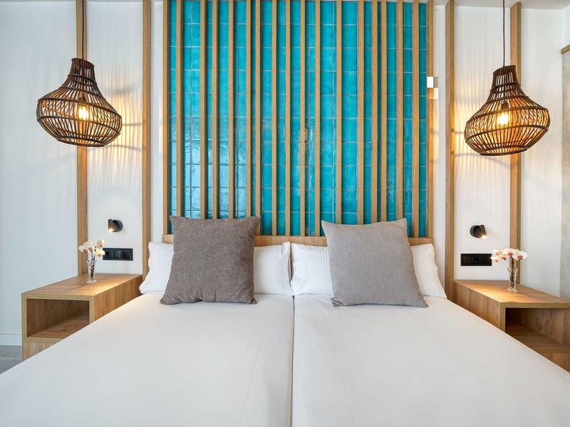 Modern hotelkamer met twee eenpersoonsbedden, stijlvolle lampen en blauwe wanddecoratie.