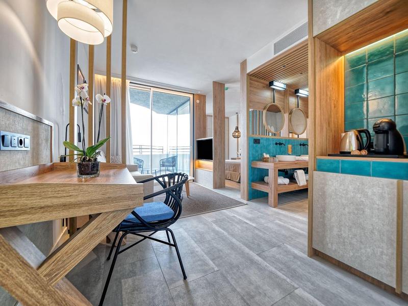Modern hotelkamer met bureau, stoel en uitzicht op balkon met zeezicht.