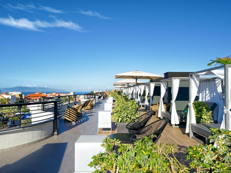Luxe hotelterras met witte cabana's, ligstoelen en uitzicht op zee onder een heldere hemel.