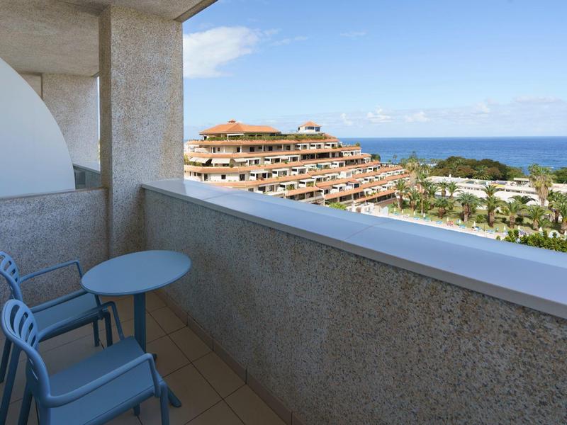 Balkon met stoelen, tafel en zeezicht bij een hotel met uitzicht op groen en gebouwen.