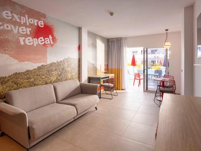 Světý hotelový pokoj s pohovkou, psacím stolem a výhledem na balkon.