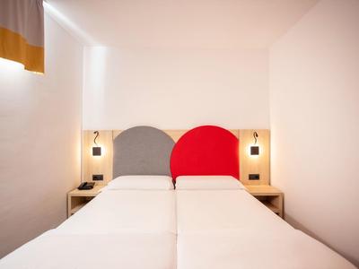 Dvě jednolůžka s barevnými kulatými čely v jednoduchém bílém pokoji