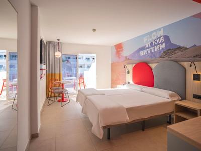 Moderní hotelový pokoj se dvěma postelemi, nástěnným uměním a balkonem s posezením.