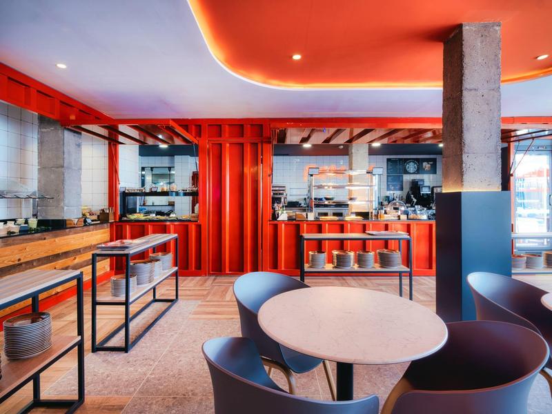 Moderní hotelová lounge s kulatými stoly, křesly a červenými zdmi a stropem.