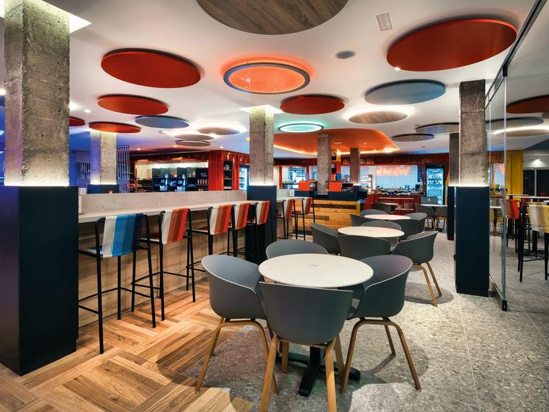 Moderní hotelový bar s barevnými stropními panely, vysokým barem a útulnými posezeními