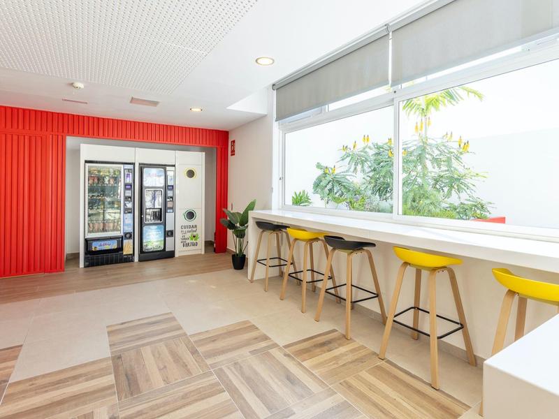 Moderní hotelová kavárna s červenými stěnami, posezením a automaty.