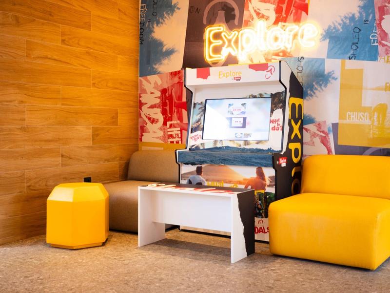 Pohodlný herní koutek se žlutým posezením a arkádovou hrou v moderním hotelovém lobby.