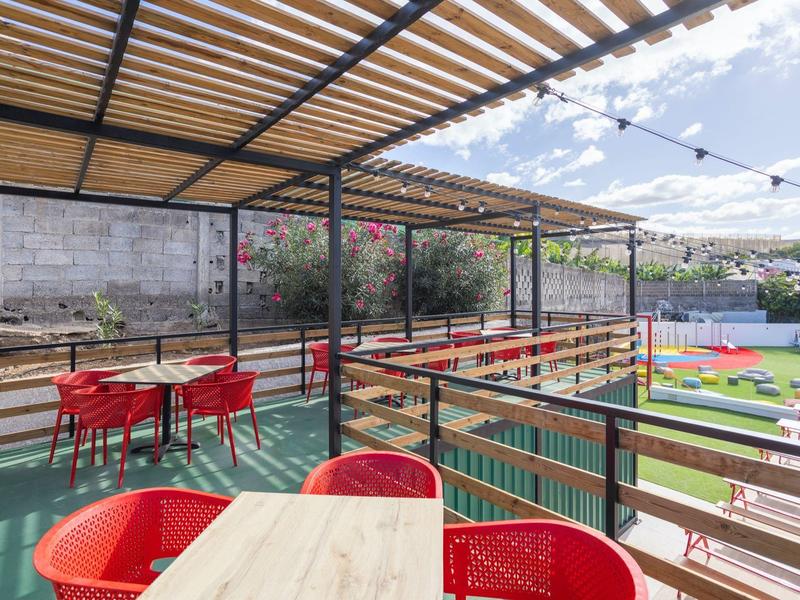 Zastřešená terasa s červenými židlemi s výhledem na zelené pole a vzdálené budovy.